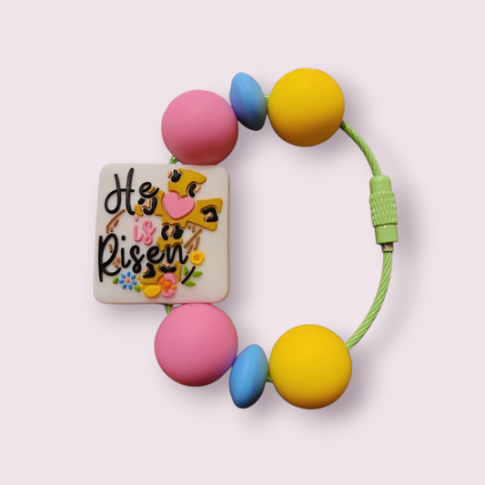 Colorful beaded bracelet with 'He is Risen' charm, pink, yellow, blue beads, green cord